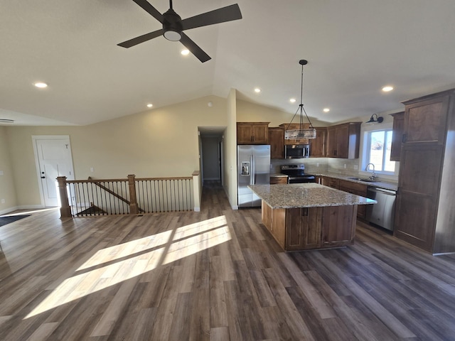 kitchen with appliances with stainless steel finishes, sink, decorative light fixtures, dark hardwood / wood-style floors, and a kitchen island