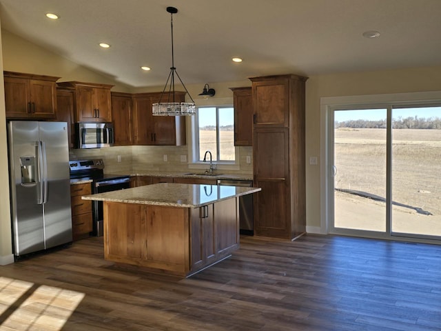 kitchen with appliances with stainless steel finishes, tasteful backsplash, sink, decorative light fixtures, and a kitchen island