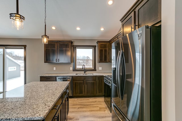 kitchen featuring sink, light stone counters, pendant lighting, appliances with stainless steel finishes, and light wood-type flooring