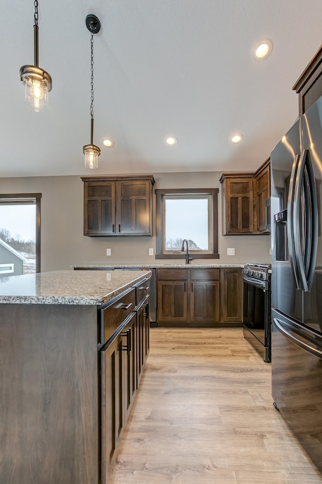 kitchen featuring light stone countertops, stainless steel fridge, pendant lighting, light hardwood / wood-style floors, and black range