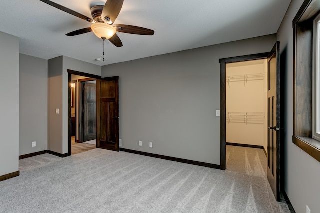 unfurnished bedroom featuring a walk in closet, ceiling fan, a closet, and light colored carpet