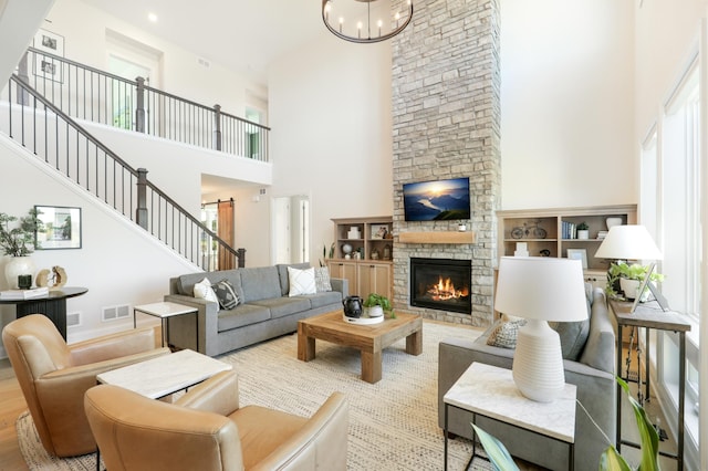 living room featuring light hardwood / wood-style floors, a towering ceiling, a stone fireplace, and a notable chandelier