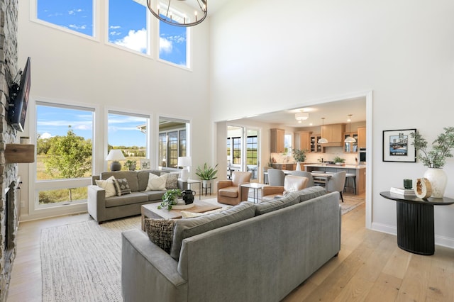 living room featuring a fireplace, a notable chandelier, a towering ceiling, and light wood-type flooring