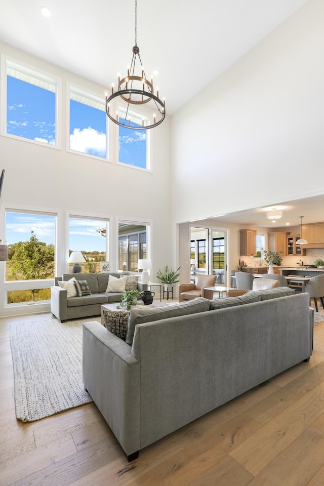 living room with a towering ceiling, a chandelier, and light wood-type flooring