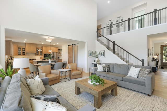 living room with a towering ceiling, light hardwood / wood-style flooring, a barn door, and an inviting chandelier