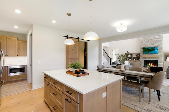 kitchen with decorative light fixtures, a center island, light wood-type flooring, appliances with stainless steel finishes, and light stone countertops