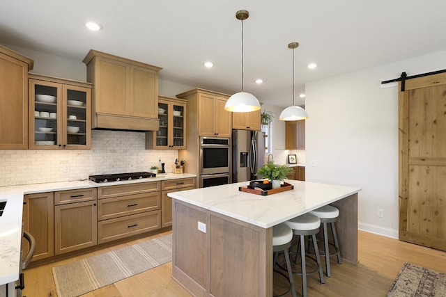 kitchen featuring a barn door, a center island, light hardwood / wood-style flooring, hanging light fixtures, and appliances with stainless steel finishes