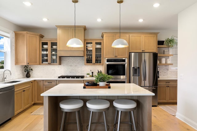 kitchen featuring light hardwood / wood-style floors, stainless steel appliances, a kitchen island, pendant lighting, and sink