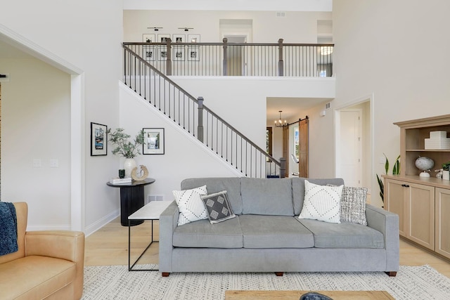 living room with light hardwood / wood-style flooring, a towering ceiling, and a notable chandelier