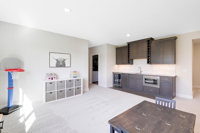 kitchen with light carpet, stainless steel microwave, backsplash, beverage cooler, and sink