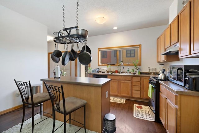 kitchen featuring gas stove, sink, dark hardwood / wood-style floors, a breakfast bar, and a kitchen island