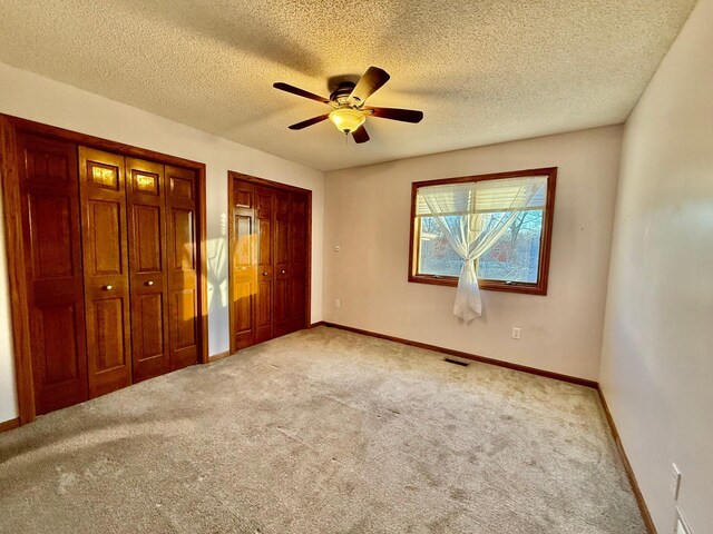 unfurnished bedroom featuring a textured ceiling, ceiling fan, light carpet, and multiple closets