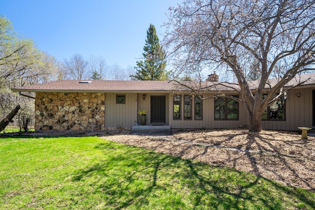 view of front facade featuring a shingled roof, a chimney, a front lawn, and stone siding