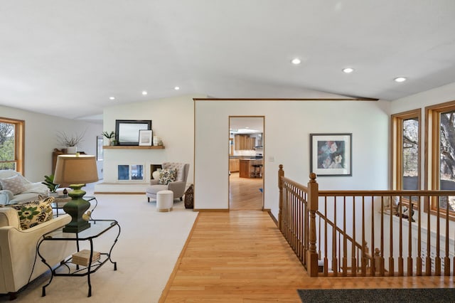 living area with a glass covered fireplace, recessed lighting, light wood-style flooring, and lofted ceiling