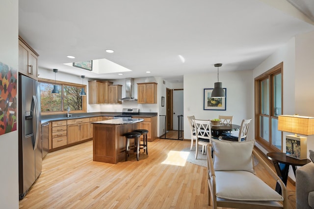 kitchen featuring light wood-type flooring, wall chimney exhaust hood, a sink, a skylight, and stainless steel appliances