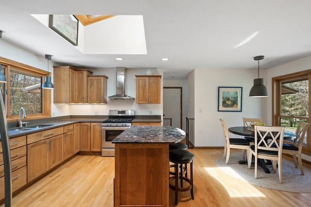 kitchen featuring stainless steel gas range, wall chimney exhaust hood, light wood finished floors, a wealth of natural light, and a skylight