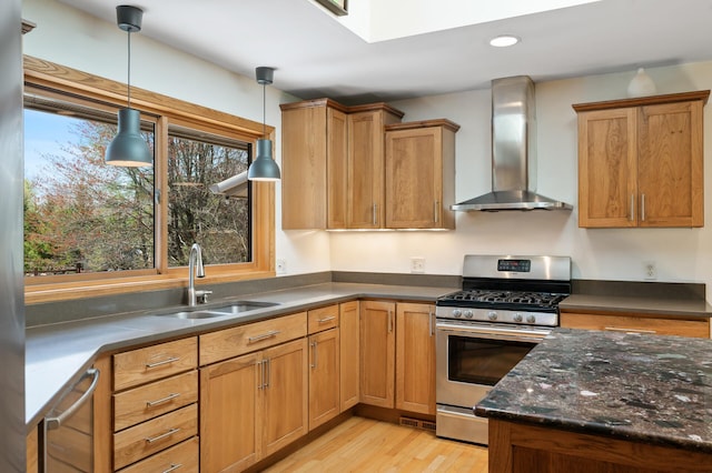 kitchen with a sink, gas stove, light wood-style floors, wall chimney exhaust hood, and decorative light fixtures