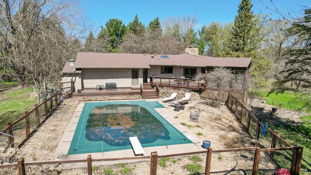 back of house with a wooden deck, a patio, a fenced backyard, a chimney, and a fenced in pool