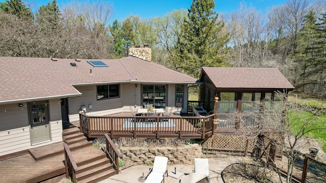rear view of property with roof with shingles, a chimney, and a deck