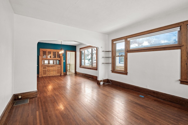 empty room featuring baseboards, visible vents, arched walkways, and dark wood-type flooring