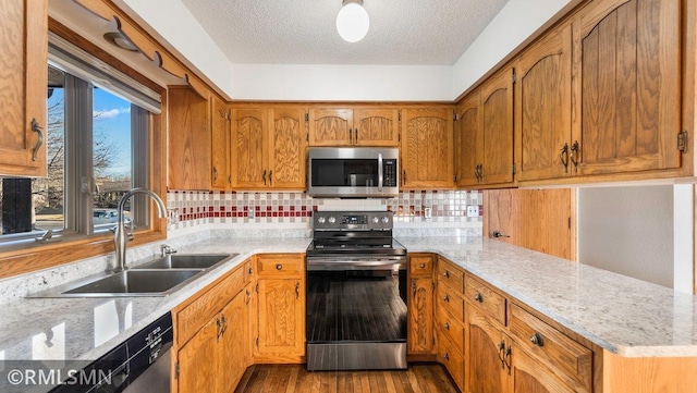 kitchen with light stone countertops, sink, a textured ceiling, appliances with stainless steel finishes, and hardwood / wood-style flooring