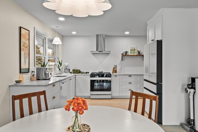 kitchen with gas range oven, wall chimney range hood, a sink, stainless steel dishwasher, and freestanding refrigerator