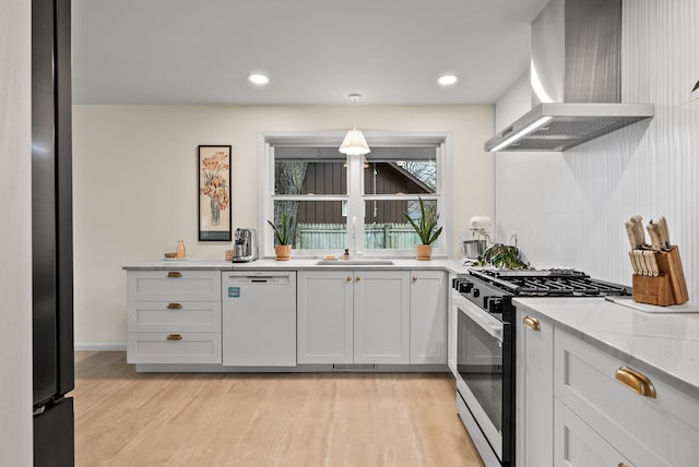 kitchen featuring gas range, wall chimney range hood, dishwasher, light wood-type flooring, and light stone countertops