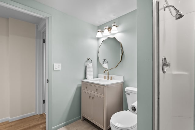 bathroom featuring toilet, wood finished floors, a shower, vanity, and baseboards