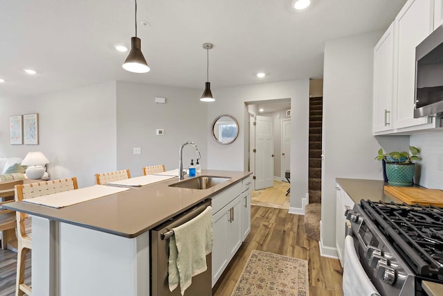 kitchen featuring a kitchen bar, appliances with stainless steel finishes, hanging light fixtures, sink, and white cabinets