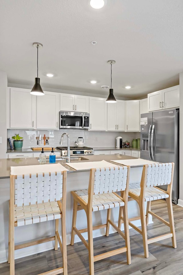 kitchen featuring decorative light fixtures, white cabinetry, appliances with stainless steel finishes, and light wood-type flooring