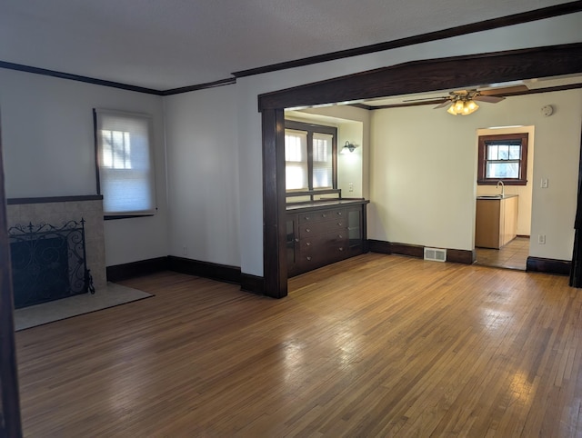 unfurnished living room with sink, wood-type flooring, ornamental molding, ceiling fan, and a fireplace