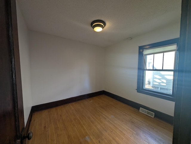 spare room with a textured ceiling and light hardwood / wood-style floors