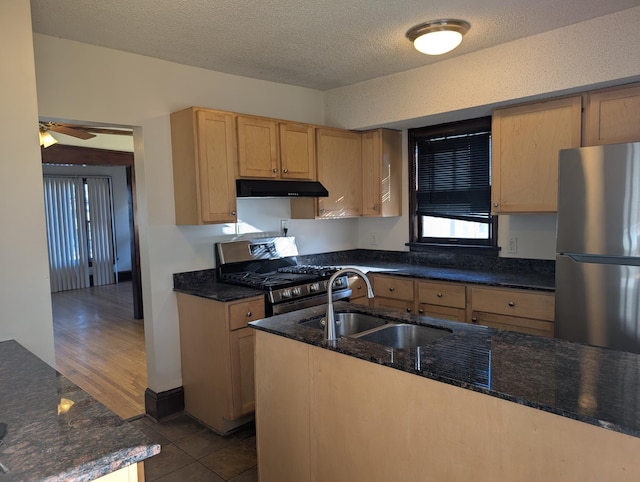 kitchen featuring stainless steel appliances, sink, dark stone countertops, and light brown cabinetry