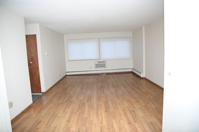 empty room featuring hardwood / wood-style floors, a textured ceiling, a baseboard radiator, and a wall unit AC