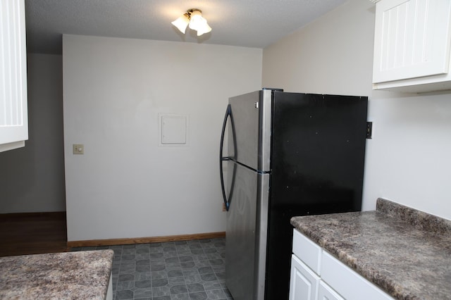 kitchen with a textured ceiling, white cabinetry, and stainless steel refrigerator