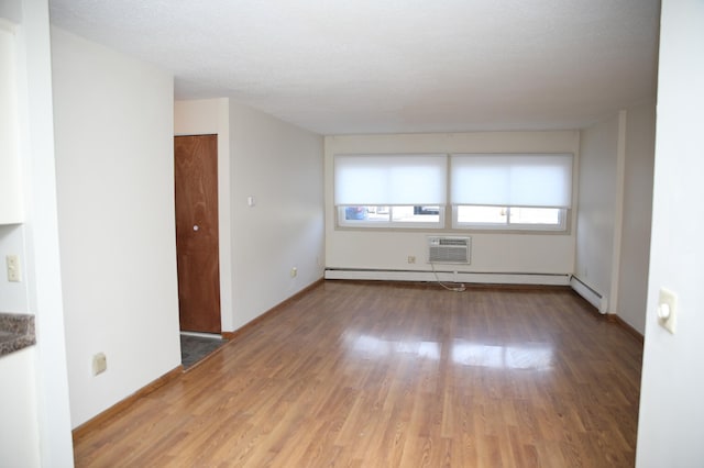 empty room featuring wood-type flooring, a textured ceiling, a baseboard radiator, and a wall mounted AC