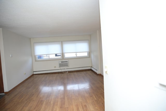 spare room featuring wood-type flooring, a textured ceiling, a wall unit AC, and a baseboard radiator