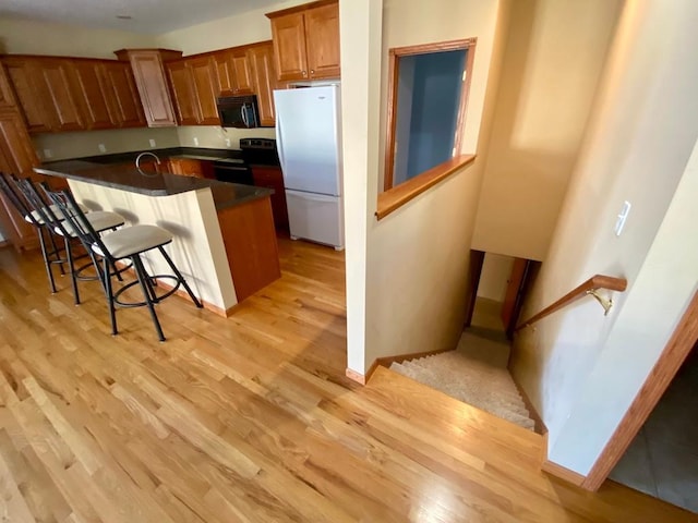 kitchen with light wood-type flooring, a kitchen bar, fridge, and electric stove