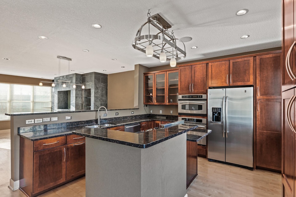 kitchen featuring dark stone counters, stainless steel appliances, sink, hanging light fixtures, and an island with sink