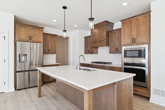 kitchen featuring tasteful backsplash, stainless steel appliances, sink, pendant lighting, and a center island with sink