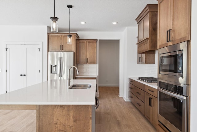 kitchen with backsplash, sink, hanging light fixtures, an island with sink, and stainless steel appliances