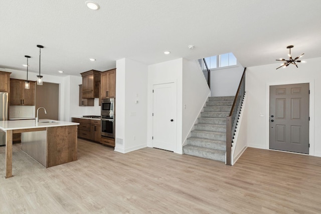 kitchen featuring appliances with stainless steel finishes, backsplash, sink, pendant lighting, and a center island with sink