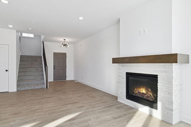 unfurnished living room featuring light wood-type flooring, a brick fireplace, and a notable chandelier