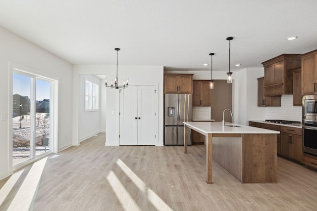 kitchen with sink, hanging light fixtures, appliances with stainless steel finishes, and an island with sink