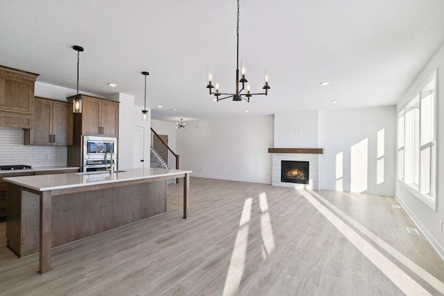 kitchen featuring pendant lighting, an island with sink, appliances with stainless steel finishes, tasteful backsplash, and a chandelier