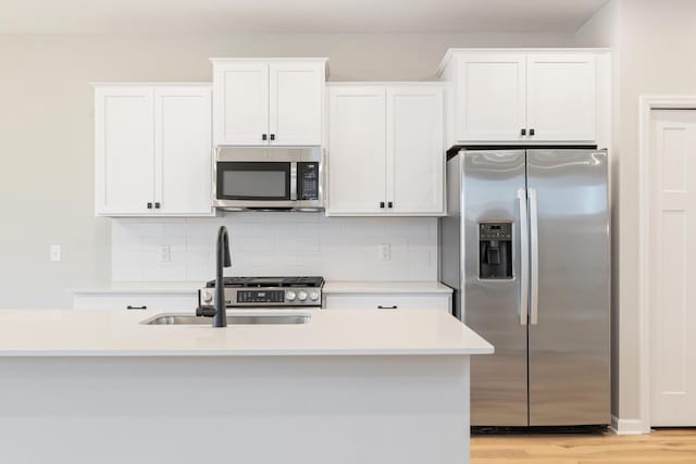 kitchen featuring appliances with stainless steel finishes, backsplash, sink, light hardwood / wood-style flooring, and white cabinets