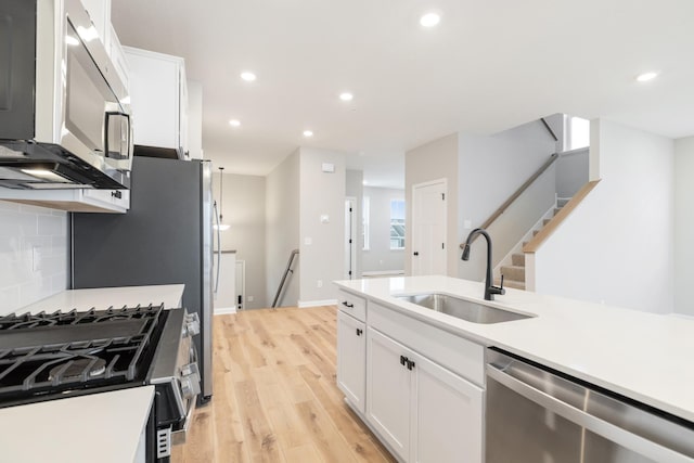 kitchen featuring appliances with stainless steel finishes, tasteful backsplash, sink, white cabinets, and light hardwood / wood-style floors