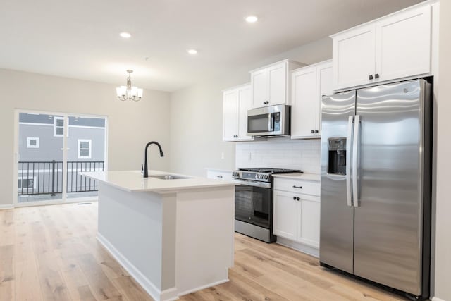 kitchen featuring tasteful backsplash, stainless steel appliances, white cabinets, hanging light fixtures, and an island with sink