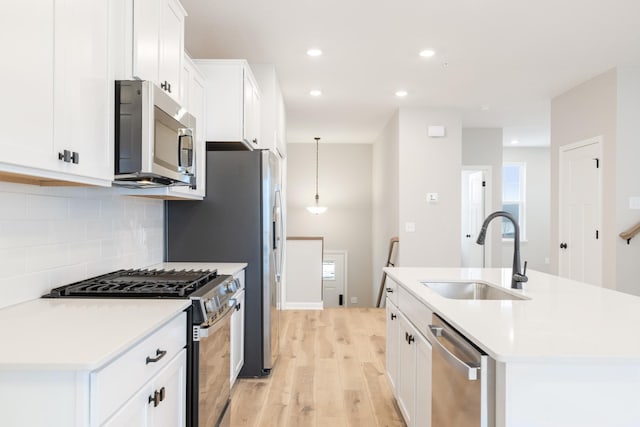 kitchen with sink, white cabinets, stainless steel appliances, and a center island with sink