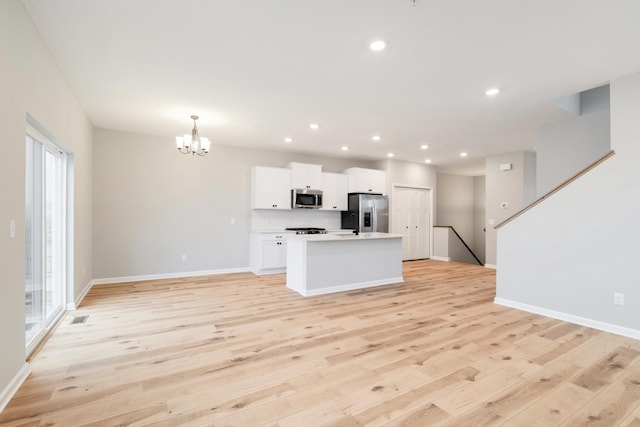 kitchen with white cabinetry, stainless steel appliances, light hardwood / wood-style flooring, a notable chandelier, and a kitchen island